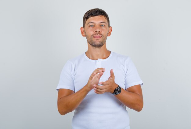 Young man preparing to claspe hands in white t-shirt and looking happy, front view.