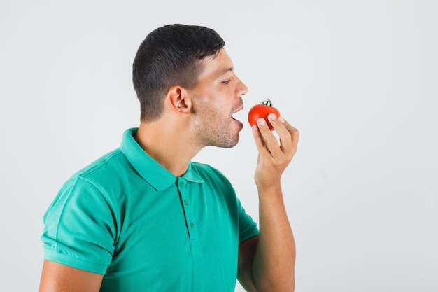 緑がかったtシャツでトマトを食べる準備をしている若い男。