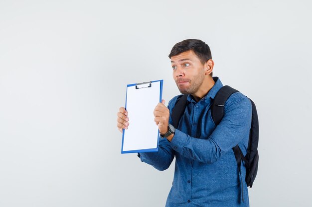 Young man presenting clipboard in blue shirt and looking scared. front view.