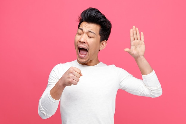 Young man pretend holding microphone keeping hand in air singing with closed eyes 