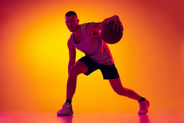 Young man professional basketball player dribbling training isolated over multicolored background in neon