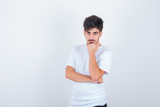 Young man propping chin on fist in t-shirt and looking confident