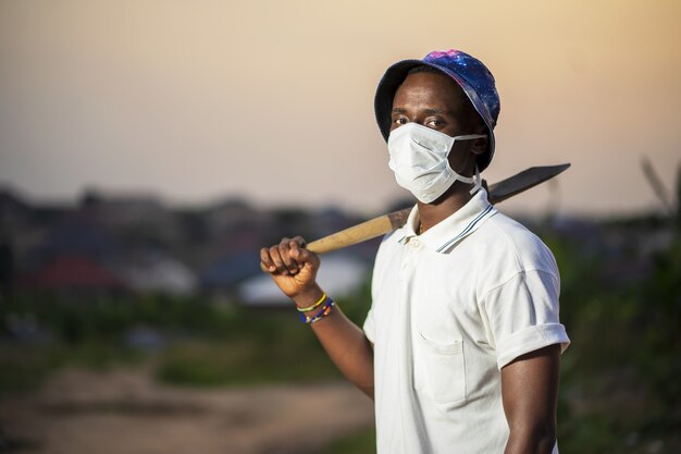 Young man in a protective face mask holding a shovel