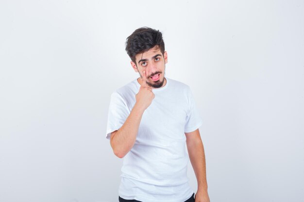 Young man pulling down his eyelid in white t-shirt and looking confident