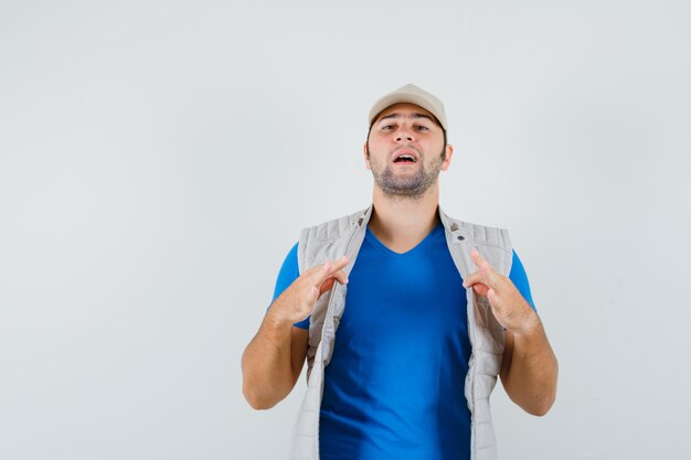 Young man pulling his open jacket in t-shirt, jacket and looking proud. front view.