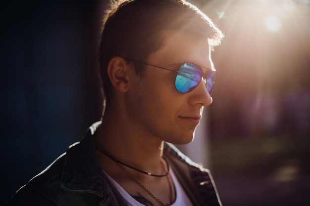 Young man puts on sunglasses standing outside