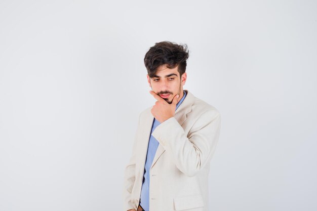 Young man putting hand on chin in blue shirt and white suit jacket and looking pensive