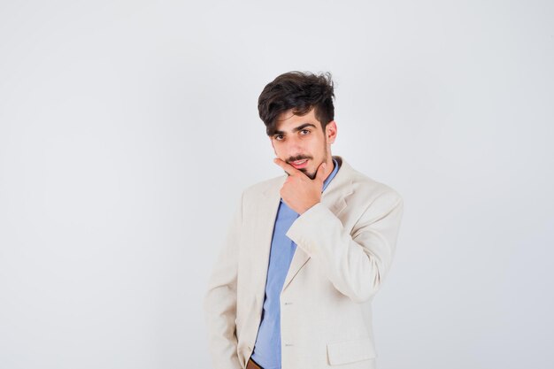 Young man putting hand on chin in blue shirt and white suit jacket and looking pensive