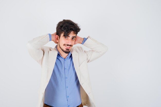 Young man putting hands behind head in blue shirt and white suit jacket and looking happy