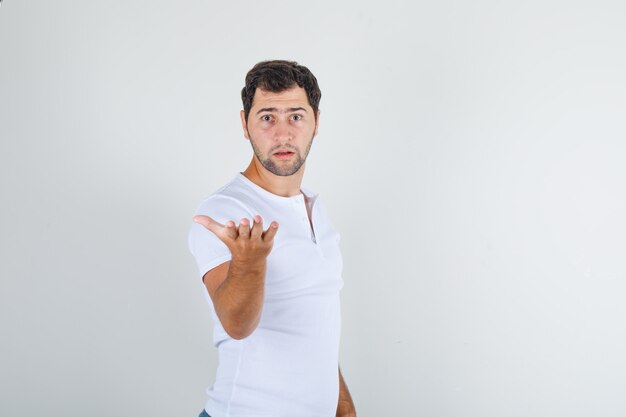 Young man raising arm in questioning gesture in white t-shirt and looking furious