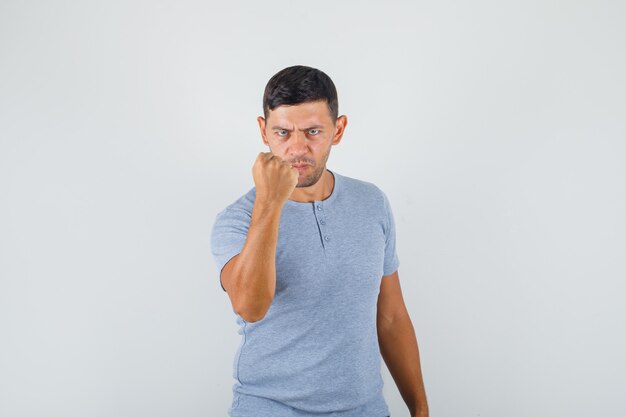 Young man raising fist with anger in grey t-shirt