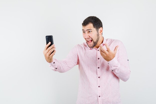 Young man raising hand on video chat in pink shirt and looking aggressive