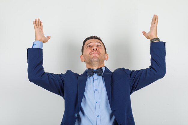 Young man raising hands and looking up in suit and looking grateful 