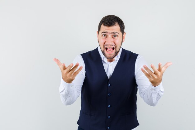 Young man raising hands in questioning manner in shirt and vest and looking nervous