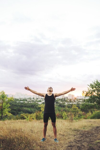 Молодой человек поднимает руки над закатным небом после тренировки