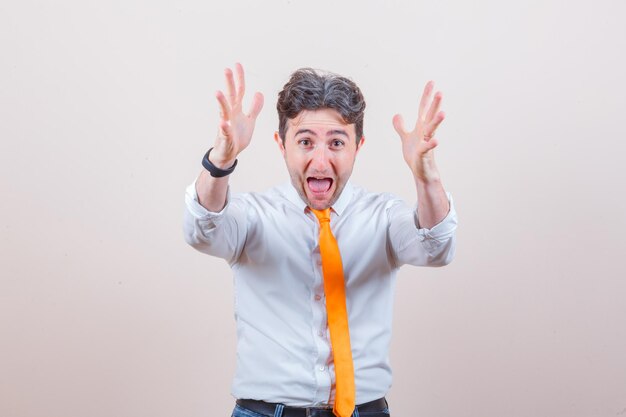 Young man raising hands while screaming in shirt, jeans and looking crazy