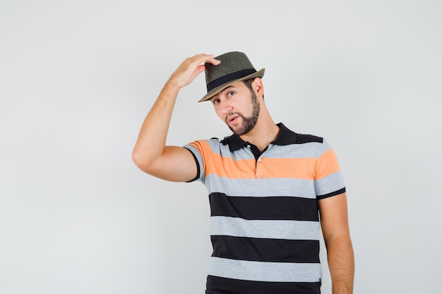 Young man raising his hat in t-shirt and looking elegant