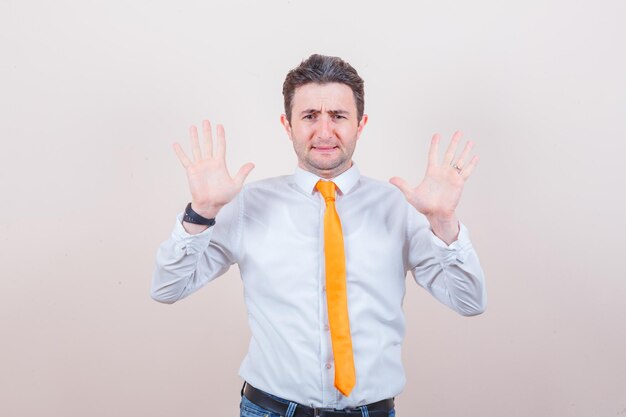 Young man raising palms in surrender gesture in white shirt