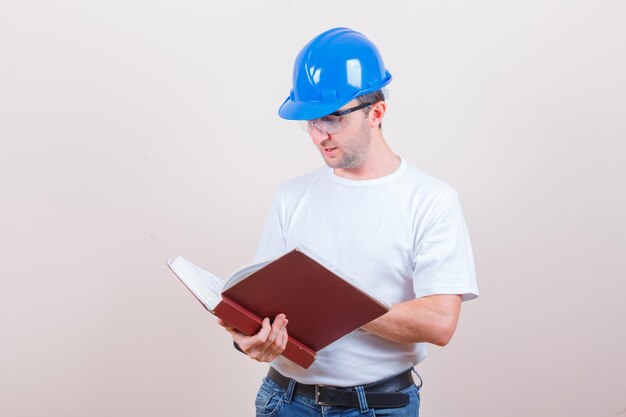 Young man reading book in t-shirt, jeans, helmet and looking busy