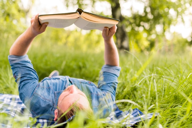 Молодой человек читает интересную книгу во время отдыха в траве