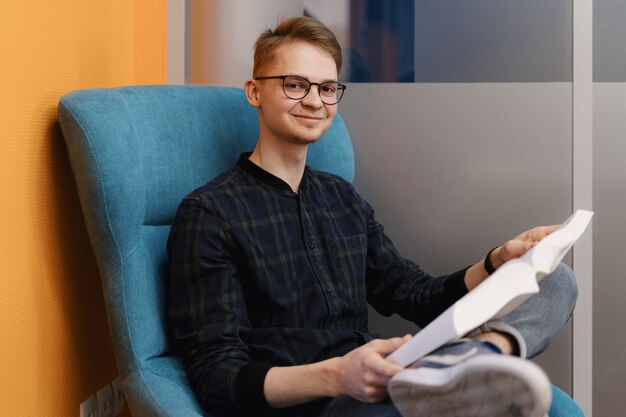 Young man reading a thick book in an armchair