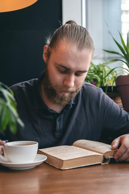 A young man reads a book over a cup of tea in a cafe