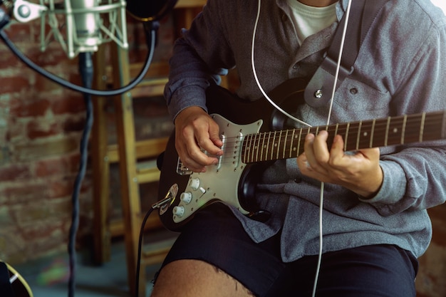 Young man recording music, playing guitar and singing at home