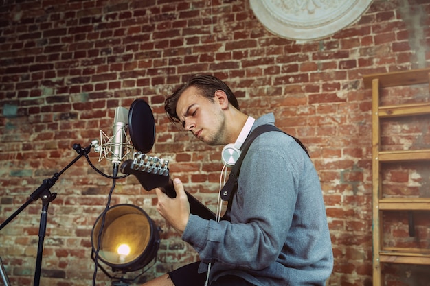 Free photo young man recording music, playing guitar and singing at home