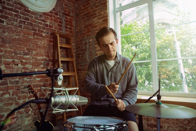 Young man recording music video blog, home lesson or song, playing drums or making broadcast internet tutorial while sitting in loft workplace or at home