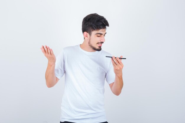 Young man recording voice message on mobile phone in t-shirt and looking confident