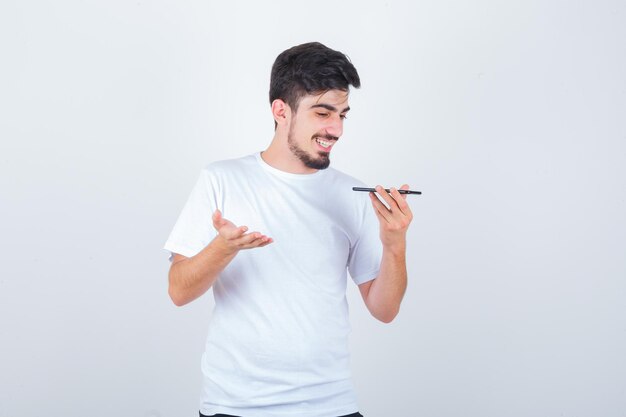 Young man recording voice message on mobile phone in t-shirt and looking happy