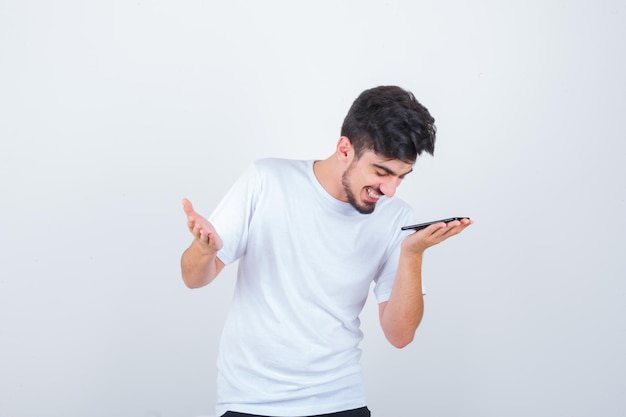 Young man recording voice message on mobile phone in t-shirt and looking positive