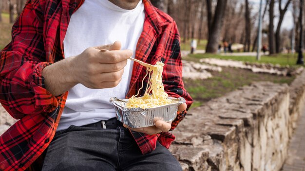 公園でパスタを食べる赤いシャツを着た若い男