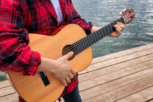 Giovane in camicia rossa che suona la chitarra vicino a un lago in un parco