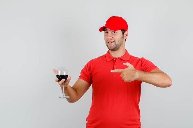빨간 티셔츠에 젊은 남자, 알코올 잔을 가리키고 기뻐 보이는 모자