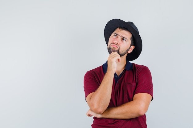 Young man in red t-shirt,hat looking away and looking focused , front view.