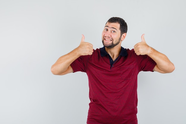 Young man in red t-shirt showing thumb up and looking happy , front view.