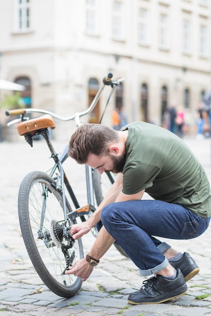 Free photo young man repairing his bicycle on street in city