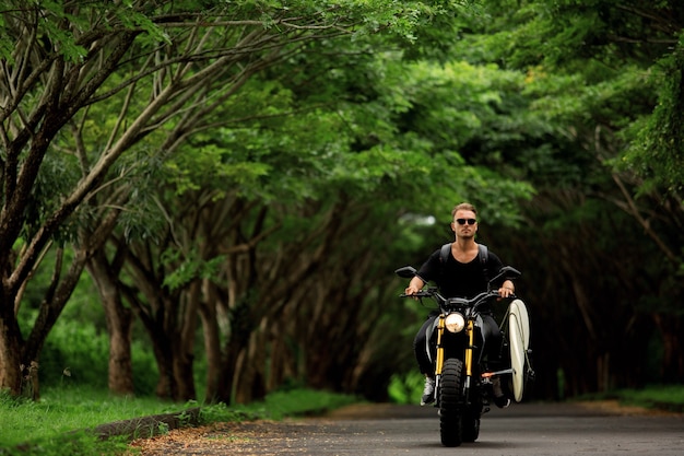 Young man rides a motorcycle with a surfboard