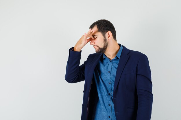 Young man rubbing eyes and nose in shirt, jacket and looking fatigued