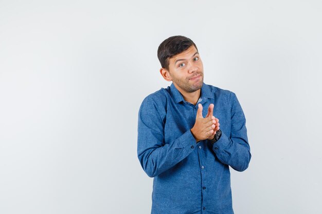 Young man rubbing palms together in blue shirt and looking jolly. front view.