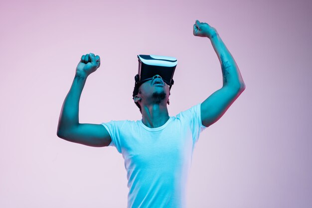 Молодой человек играет и использует VR-очки в неоновом свете на градиенте