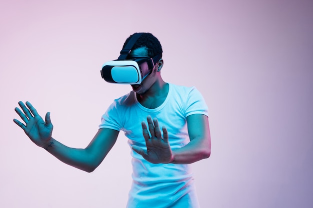 청년이 그라디언트의 네온 불빛에서 VR 안경을 연주하고 사용합니다.