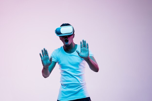 Young man's playing and using VR-glasses in neon light on gradient