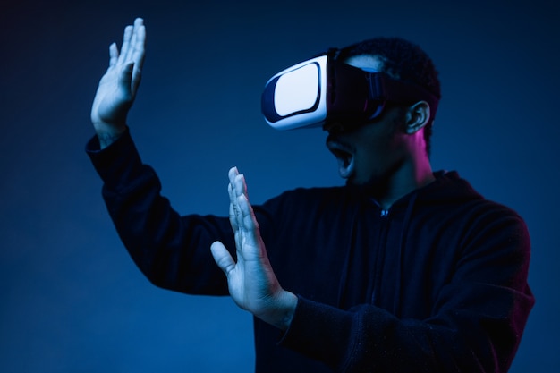 Young man's playing in VR-glasses in neon light on blue