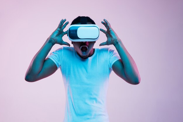 Молодой человек играет в VR-очках в неоновом свете на градиенте