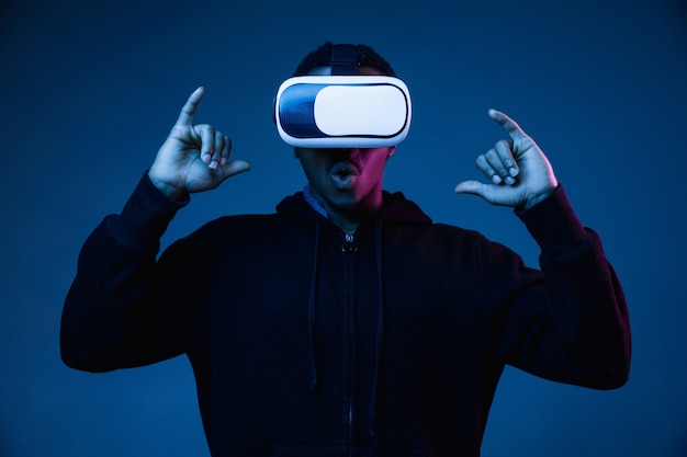 Young man's playing in VR-glasses in neon light on gradient