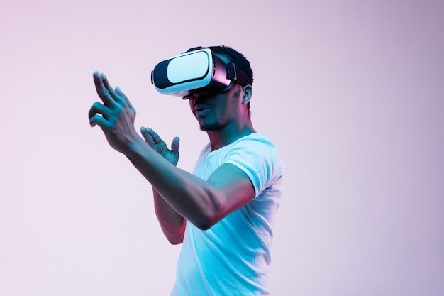 Young man's pointing and using vr-glasses in neon light on gradient