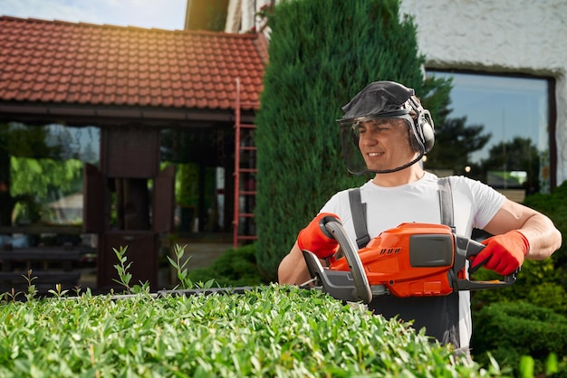 Free photo young man in safety mask and gloves shaping bushes