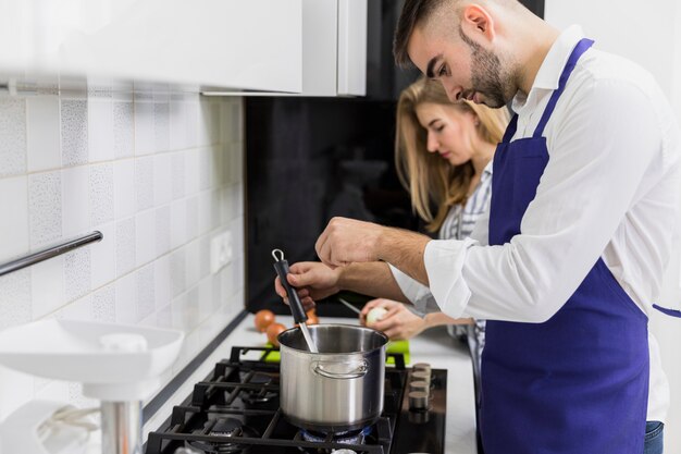 Young man salting water in pot near woman